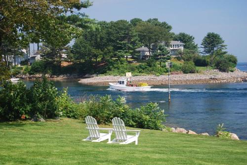two white chairs sitting on the grass with a boat in the water at Dockside Guest Quarters in York