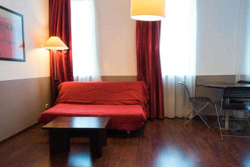 a red bed in a room with a table and curtains at Appart'City Classic Lyon Part-Dieu in Lyon