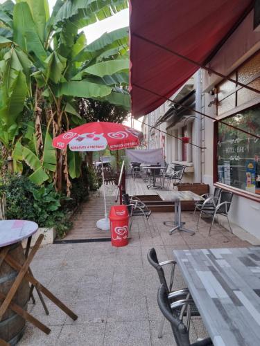 a patio with tables and chairs and a red umbrella at Hotel Café de la Gare in Sainte-Foy-la-Grande