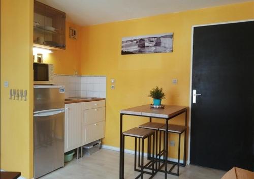 une cuisine avec des murs jaunes et une petite table avec des tabourets dans l'établissement Appartement à 50 m de la plage avec WIFI, à Villers-sur-Mer