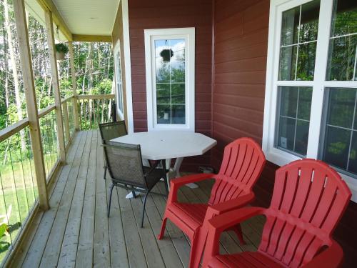 a porch with two red chairs and a white table at The Fiddle and the Sea Bed and Breakfast in Port Hood