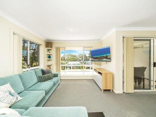 a living room with a blue couch and a flat screen tv at Kalimna by Experience Jervis Bay in Vincentia