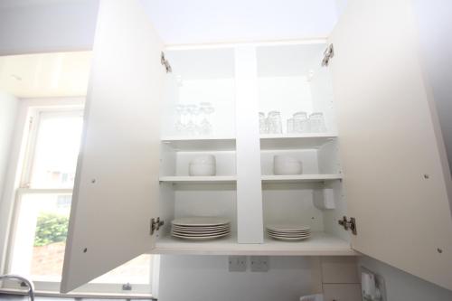 a kitchen with white cabinets and plates on shelves at Hillingdon Hill Court, Uxbridge in Hillingdon