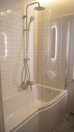 een bad met een douche en een glazen deur bij Art Apartment Szczecin II in Szczecin