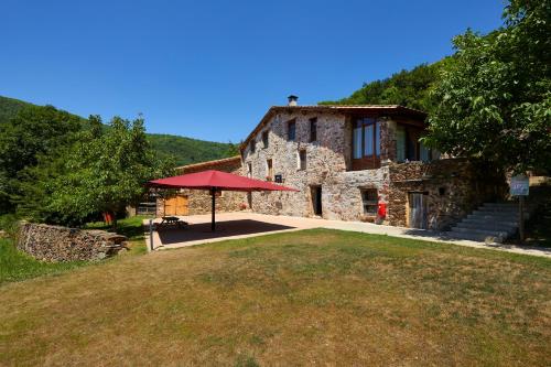 un gran edificio de piedra con una sombrilla roja delante de él en Casa Rural "Can Soler de Rocabruna" Camprodon, en Rocabruna
