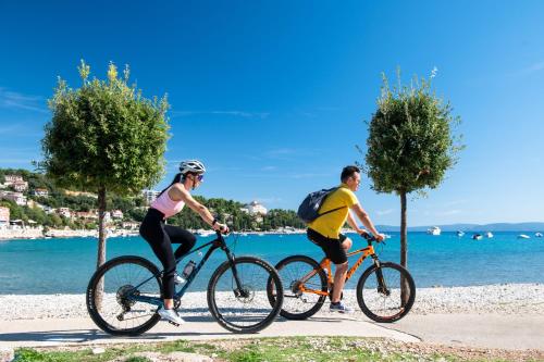 two people riding bikes on a sidewalk near the water at MASLINICA Hedera Hotel in Rabac