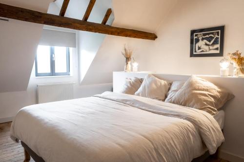 een slaapkamer met een bed met witte lakens en een raam bij Les Jardins de Jeanne in Middelkerke