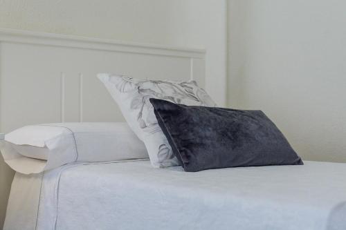 a white bed with a black pillow on it at Apartamento San Pascual 18 III en Orihuela in Orihuela