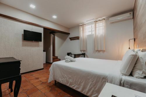 a bedroom with a white bed and a flat screen tv at Hotel Vila Bavária Petrópolis in Petrópolis