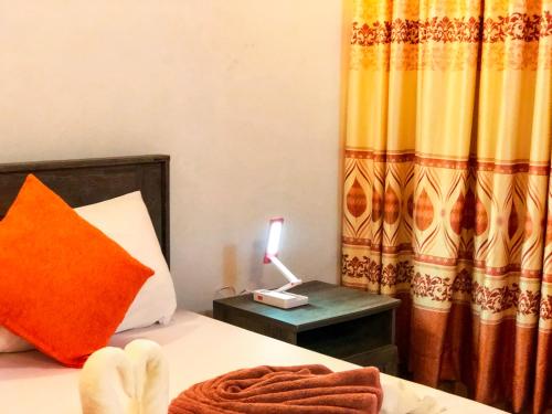 a bed with an orange pillow and a lamp on a table at Sabba Beach Suite , Fodhdhoo - Maldives in Velidhoo
