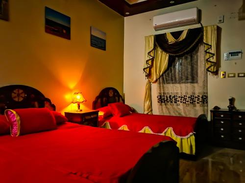 a bedroom with two beds with red sheets and a window at Safari Abu Simbel in Abu Simbel