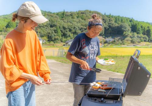 two women cooking hot dogs on a grill at Share Creative&Bed adonoan in Takeo