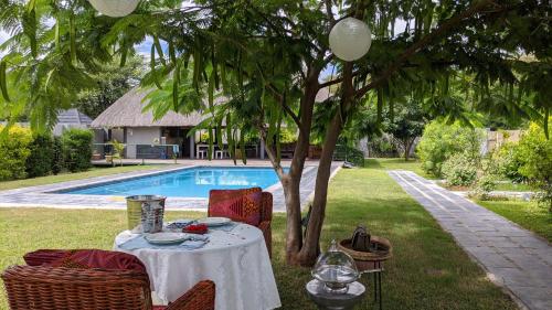a table sitting under a tree next to a pool at Sunbirds Cottage in Kasane