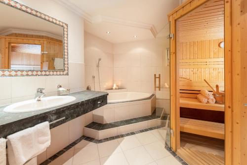 ein Badezimmer mit einem Waschbecken, einer Badewanne und einem Spiegel in der Unterkunft Appartements Alpenschlössl in Neustift im Stubaital