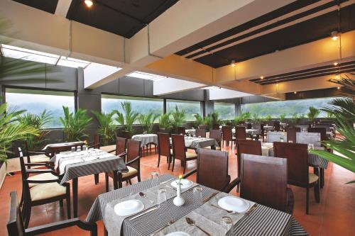ein Restaurant mit Tischen, Stühlen und Fenstern in der Unterkunft Holiday Vista Luxury Hotel and Spa, Thekkady in Thekkady