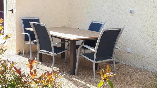 une table en bois et quatre chaises à côté d'un mur dans l'établissement Les Pucines bis Bas de villa 29 m2 luxe rez de jardin climatisation plein sud, à Six-Fours-les-Plages
