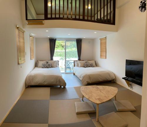 two beds in a room with a table and a tv at Villa Sunbeams ヴィラ・サンビームス in Kin