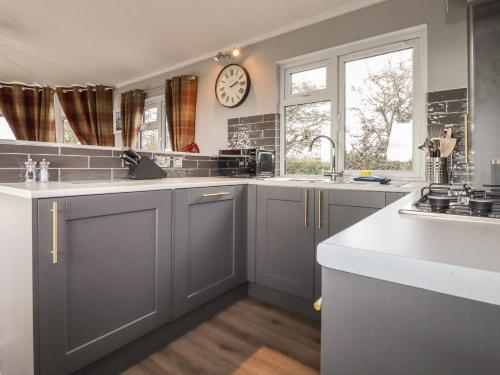 a kitchen with gray cabinets and a clock on the wall at Sycamore Lodge in Helston