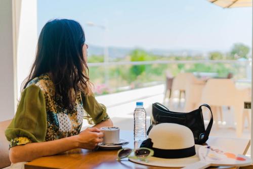 a woman sitting at a table with a hat and a cup at Hôtel Tamuda Beach in M'diq
