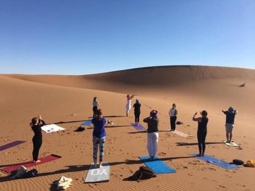 a group of people doing yoga in the desert at Camp Sahara Holidays in Mhamid