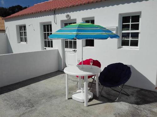 einen Tisch mit einem blauen und weißen Regenschirm und zwei Stühlen in der Unterkunft Moradia Machado in Topo