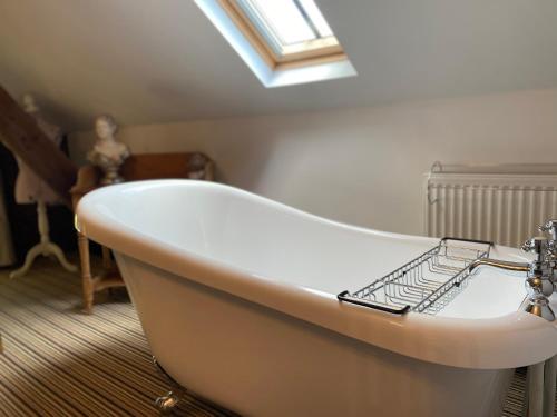 a white bath tub in a bathroom with a window at Betsey Trotwood. Historic stylish 2-bed cottage. in Blundeston