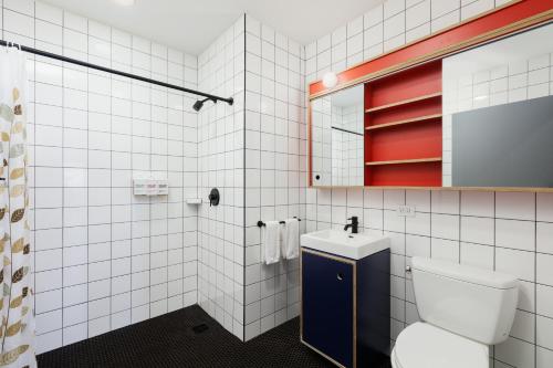 a white tiled bathroom with a toilet and a sink at Placemakr Wall Street in New York