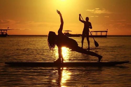 two people on a surfboard in the water at sunset at Badolina Bungalows in Nungwi