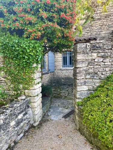 an entrance to a stone building with a bush with red flowers at Domaine de l'Enclos in Gordes