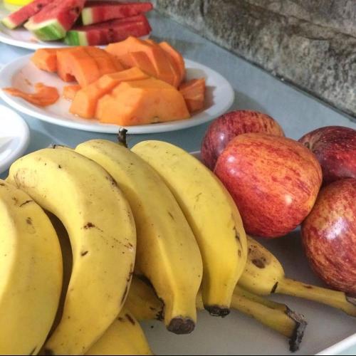 a table topped with plates of fruit and bananas and apples at Pousada Nascente Pequena in Guapimirim