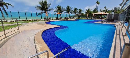a swimming pool with blue water and palm trees at Flat Tabatinga Nord, vista para o mar in Conde