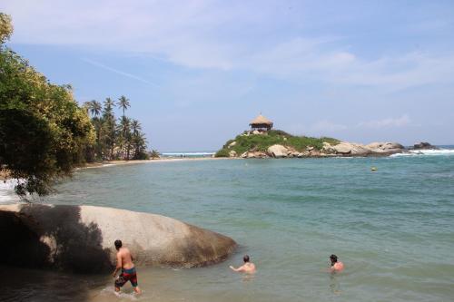three people swimming in the water on a beach at HOSTAL MIRADOR dentro del parque tayrona in El Zaino
