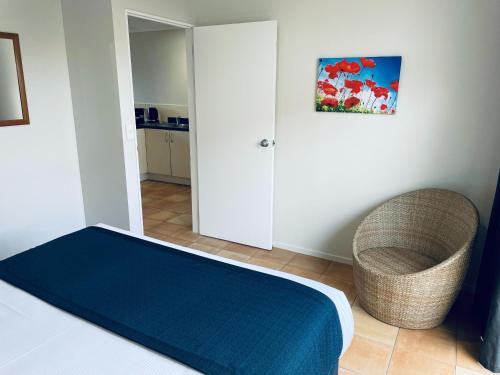 a bedroom with a bed and a chair and a mirror at Cottage Park Thermal Motel in Tauranga