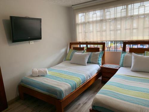 two beds in a room with a tv on the wall at Casa Bachué Hotel Boutique in Chía