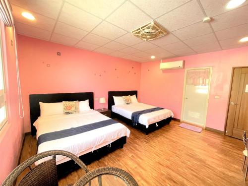 two beds in a room with pink walls and wooden floors at 台東新港民宿 in Chenggong