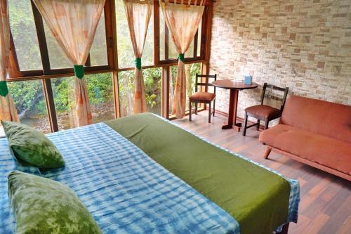 Un dormitorio con una cama y una mesa y ventanas. en La Quinta Sarapiqui Lodge, en Sarapiquí