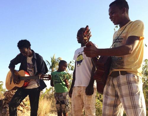 a group of men standing around a man playing a guitar at Mafu Haus in Inhambane