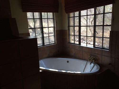 a bath tub in a bathroom with two windows at Lituba Place in Marloth Park