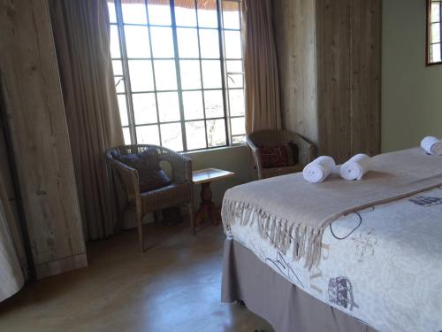 a bedroom with a bed and two chairs and a window at Lituba Place in Marloth Park