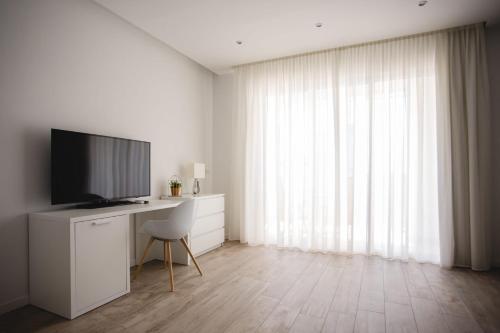 Habitación blanca con escritorio, TV y ventana. en Hotel Speranza en Lido di Jesolo