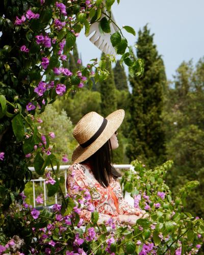 a woman wearing a hat sitting in a garden with flowers at Hotel Villa Florida & Suite Apartments in Gardone Riviera