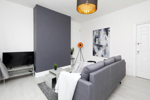 a living room with a gray couch and a tv at Your Sheffield Stays - Spacious 5 Bedroom House in Sheffield