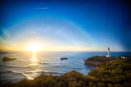 uma vista para o oceano com um farol e o pôr-do-sol em Les Echappées Belles - Studio du phare em Biarritz