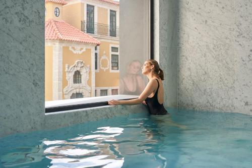 una mujer sentada en una piscina mirando por la ventana en PortoBay Flores, en Oporto