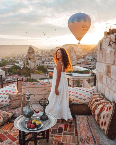 a woman standing on a balcony with a hot air balloon at Zara Cave Hotel in Goreme
