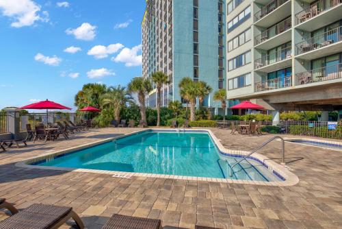 a swimming pool with tables and chairs and a building at 2-Bedroom Carolina Dunes Condo with Private Balcony and Ocean Views in Myrtle Beach