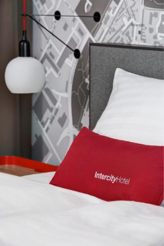 a red pillow on a white bed with a wall at IntercityHotel Zürich Airport in Rümlang