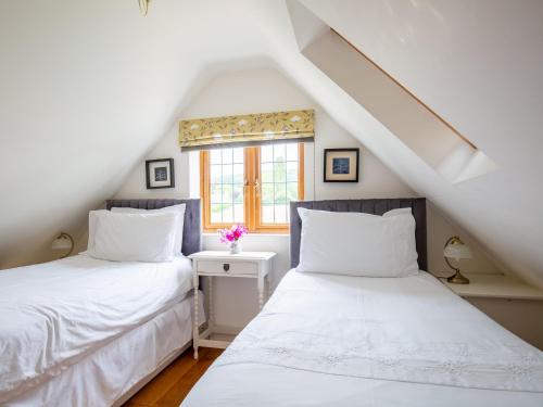 two beds in a attic room with a window at Kingfisher Cottage in Winchcombe