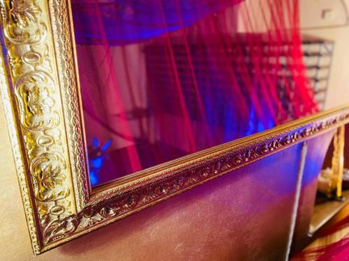 a gold picture frame on a wall with red curtain at La Cave Rouge - Secret wine cellar in the center in Florence