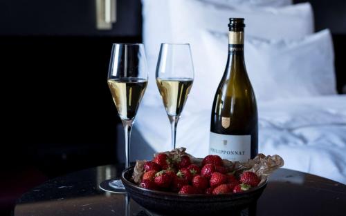 a table with two glasses of wine and a bowl of strawberries at Radisson Collection, Strand Hotel, Stockholm in Stockholm